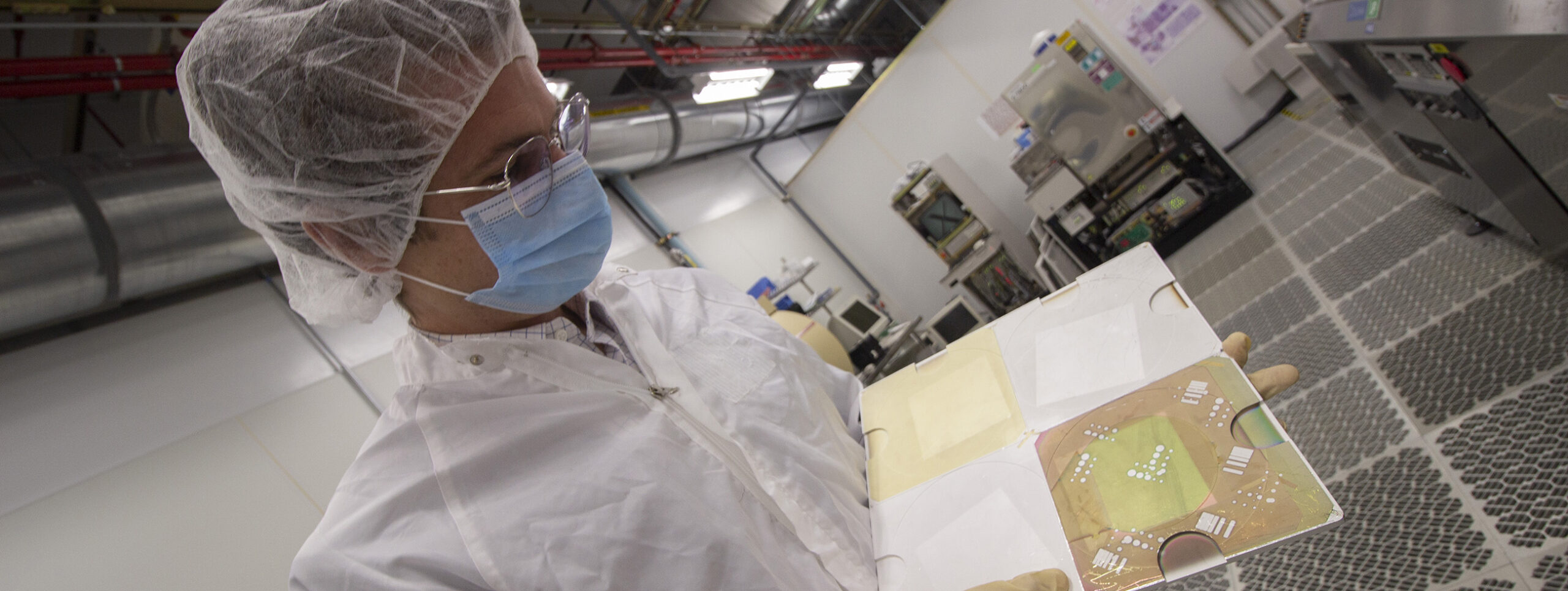 A faculty member examines a photovoltaic device in a cleanroom.